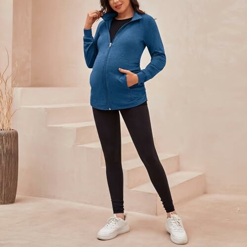 Pregnant woman in blue jacket and black leggings standing indoors