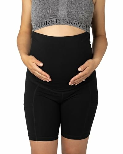 Pregnant woman wearing black maternity biker shorts and gray top.