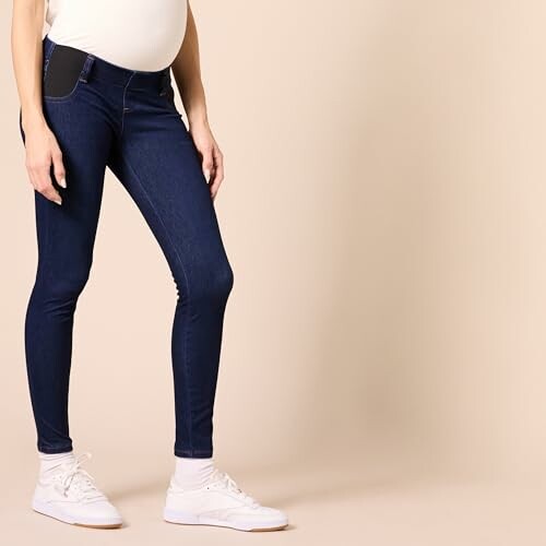 Side view of a person wearing maternity jeans and white sneakers.