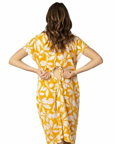 Woman tying the back of a yellow floral dress.